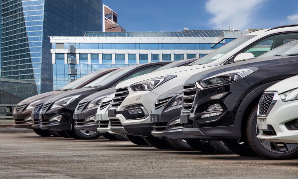 Row of modern SUVs parked in front of blue city skyscrapers.